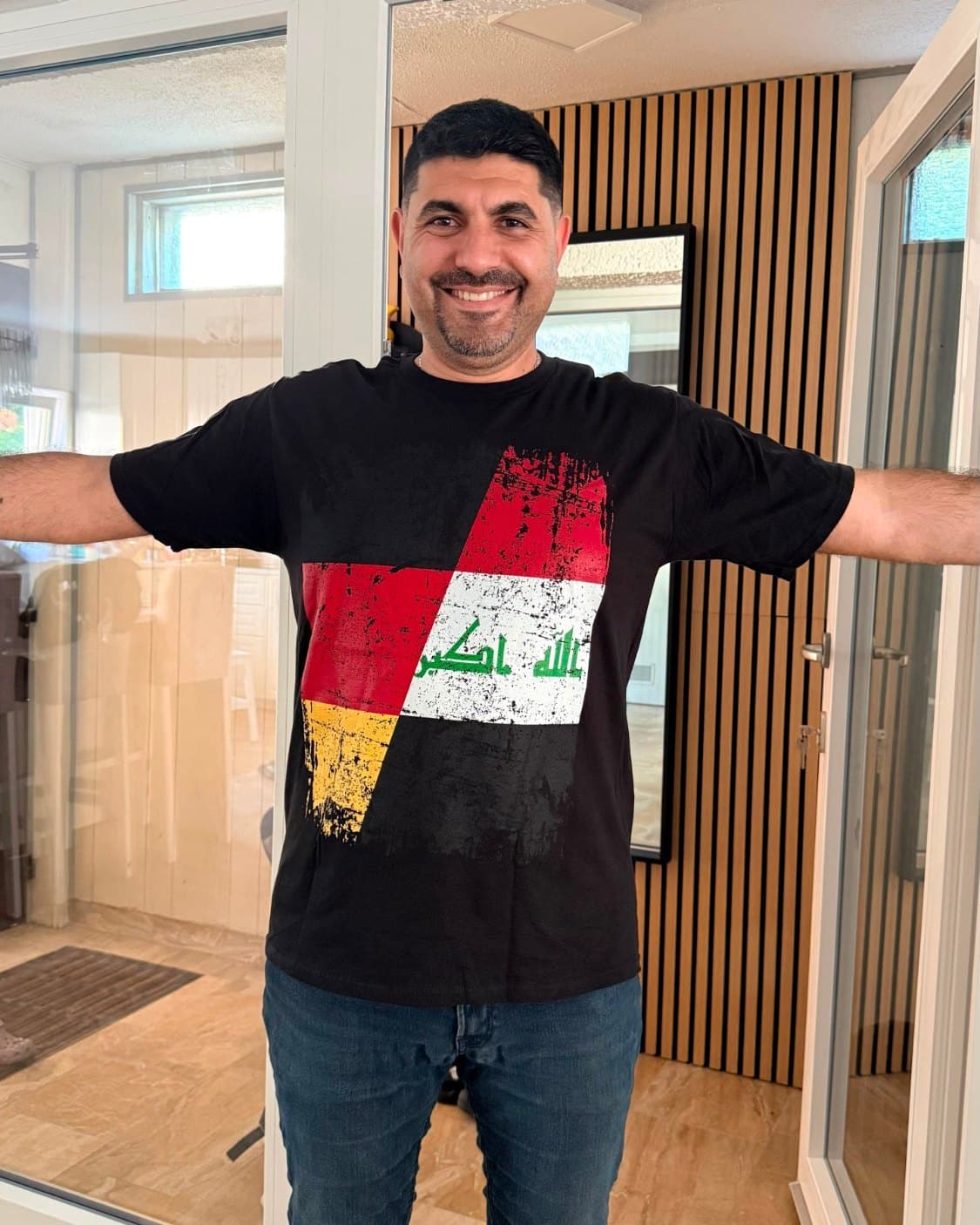 Husam Noaman with open arms, wearing a black T-shirt with the German and Iraqi flags