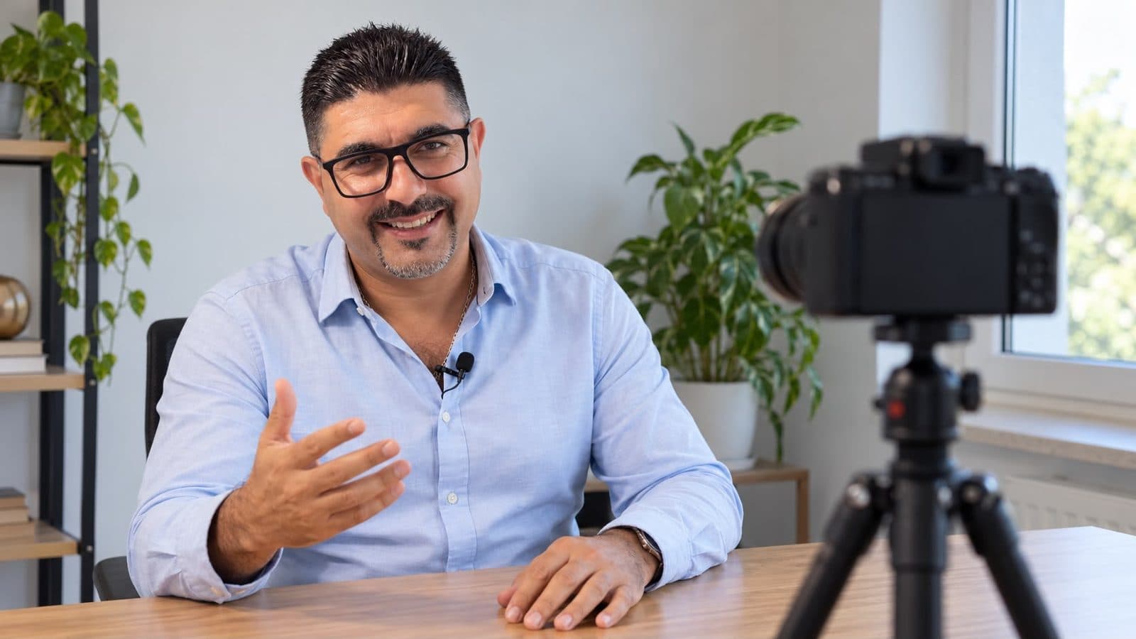Husam Noaman talking and gesturing in front of a camera on a tripod, with a small clip-on microphone